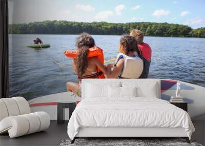 People sitting on a boat and tubing on an inland lake Wall mural