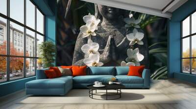 A stone Buddha statue with hands folded in a prayer pose, holding white orchid flowers around its neck and face. The background is a tropical garden with natural light. It is a professionally photogra Wall mural