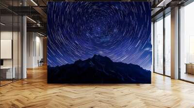 The starry sky is full of circular long exposures, with star trails visible in the night sky over mountains. A long time exposure photo captures stars spinning around the North Star Polaris, creating  Wall mural