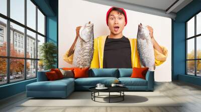 A man in black t-shirt and yellow jacket holding two huge fish in both hands, looked at the camera in surprise, good luck concept, copy space, high quality photo Wall mural