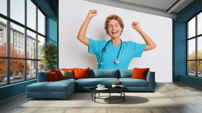 Cheerful female doctor dances with pleasure in light studio raising her arms up and smiling, good doctor concept, copy space Wall mural