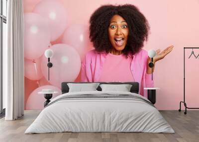 Portrait shot of positive emotional woman with surprised expression, holds delicious cake with burning candles, prepares for the party, poses over pink wall Wall mural