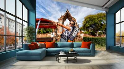 Young asian female traveler with backpack traveling with standing on taxi or Tuk Tuk and happy fun with old temple (Wat Mahathat) background, Ayutthaya Province, Thailand Wall mural