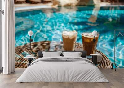 Two glasses of iced coffee on a table near a brown sun lounger in a pool with blue water, view from the hotel Wall mural