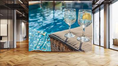 Two glasses of water with a lemon slice in them are on a table by a pool Wall mural