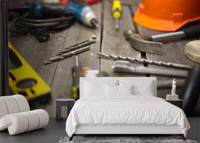 Tools on the table.  On the table is: drills on wood and metal, a hammer.  In no focus: a building level, a tape-measure, a drills on concrete, chisel, screwdriver, helmet, Wall mural