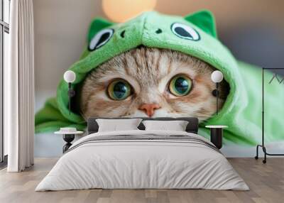 A cat wearing a green frog costume is laying on a bed Wall mural