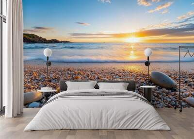 The beach is covered in small rocks and the sun is setting in the distance Wall mural