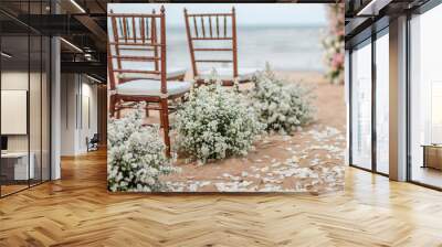 Wedding wooden chairs decorated with flowers. Rustic aisle chairs standing on sand for ceremony on the beach. Natural, shabby, boho wedding decor Wall mural