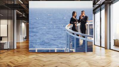 Young beautiful elegant couple standing on a deck of cruise ship wearing formal black evening gown and tuxedo. VIP holiday, honeymoon or proposal Wall mural