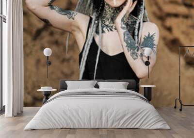 Beautiful sexy woman in black underwear. The body is covered with many tattoos. Dreadlocks on the head . Posing against sandy career and black fabric. Wall mural