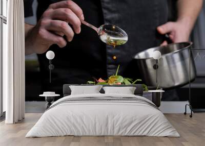 Close-up of the hands of a male chef on a black background. Pour sauce from the spoon on the salad dish. Wall mural