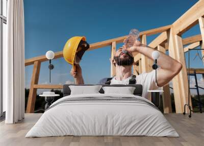 the man builder sits on the edge of the roof of the frame house, in a yellow helmet and gray overall Wall mural