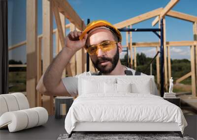 The man is a builder on the roof of a wooden frame house. Wall mural