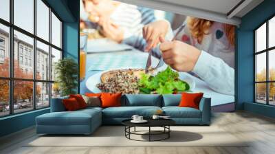 Close up photo of hands of child girl eating healthy dinner with salad, quinoa and fish Wall mural