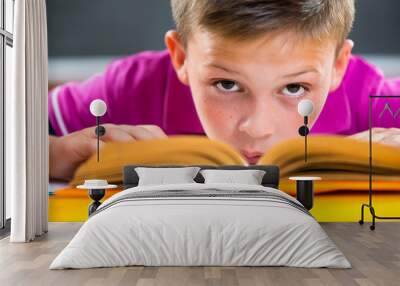 Cute schoolboy reading in classroom Wall mural