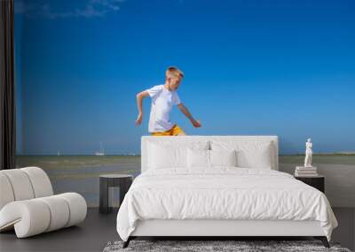 Happy teen boy playing with ball on beach at summer sunny day with blue sky Wall mural