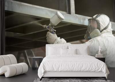 A man in a white uniform applies paint with a spray gun on a metal product. Wall mural