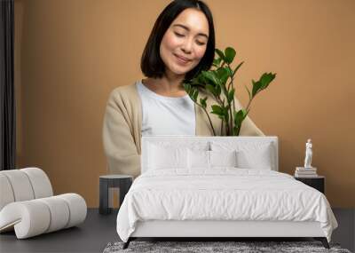 Portrait of delighted female person holding flower plant in pot while posing with closed eyes Wall mural