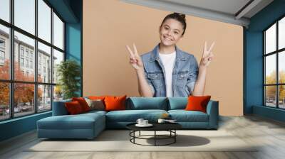 Positive, smiling teenage girl showing V gesture. The girl joyfully gestures on a brown background Wall mural