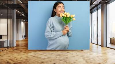 Pregnant asian woman in winter outfit smelling tulips isolated on blue Wall mural