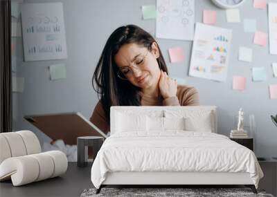 Tired girl from long work on the tablet, touches her neck, from fatigue she closed her eyes. Beautiful, young woman at the desk working in a modern office. Wall mural