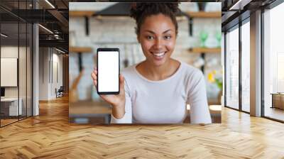 Young smiling woman sits and showing a mockup with white screen of cell telephone . - Image Wall mural