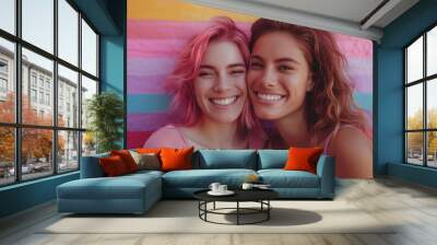 Two young women with pink and brown hair smile in front of rainbow-colored striped backdrop Wall mural