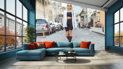 A young stylish blonde woman in a trendy outfit is walking on a European street. Street fashion Wall mural