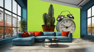 Cactus in pot with alarm clock on green studio background. Minimalism Wall mural