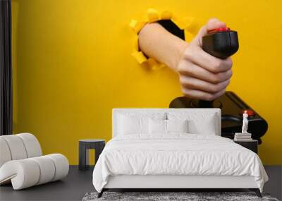 Female hand holds retro joystick through torn hole yellow paper. Concept art. Wall mural