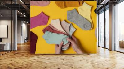 Female hands holding stack of color socks on yellow studio background. Top view Wall mural