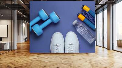 Flat lay style sport concept. Dumbbells, sneakers, jump rope, bottle of water. Sports equipment on purple background. Top view Wall mural