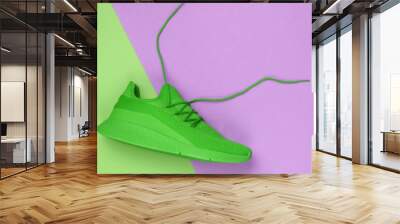 Green sports sneaker with untied laces on a green-pink paper background. Creative sport still life, minimalism. Top view Wall mural