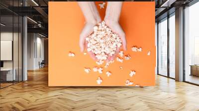 Lot of popcorn in  hands on orange background. Top view, minimalism. Wall mural