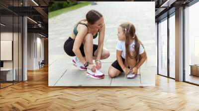 Mom runner and her little daughter tie their shoelaces before jogging outdoors. Active family concept Wall mural