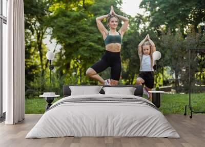 Mom with little daughter practice yoga asana pose in the park. Mom trainer,  spending time together, healthy family concept Wall mural