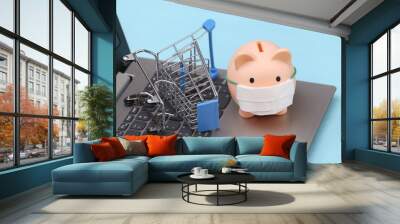 Piggy bank in medical mask with shopping trolley on laptop keyboard. Blue background. Covid-19 pandemic Wall mural