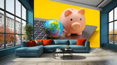 Piggy bank with globe on laptop keyboard,  yellow background. Wall mural