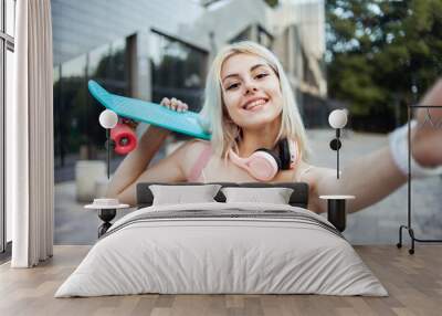 Selfie portrait of cool young smiling girl iwith skateboard n the city Wall mural