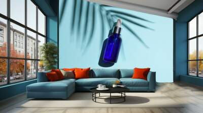 Serum bottle on blue background with palm leaf shadow. Creative beauty layout. Top view. Wall mural