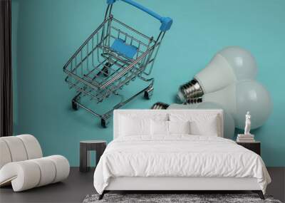 Three LED light bulbs and shopping cart on blue background. Wall mural