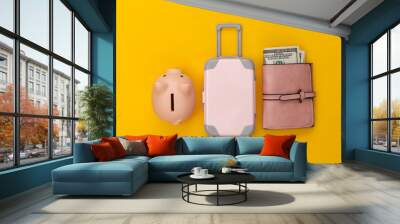 Travel flat lay. Mini plastic travel suitcase, purse and piggy bank on yellow background. Minimal style. Top view Wall mural