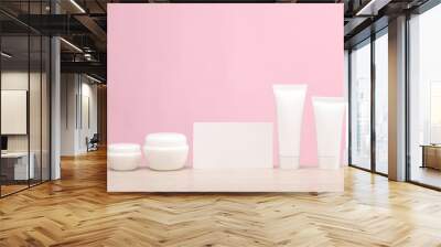 White cream tubes with jars and blank busines card on the table, pink background. Creative layout. Template for design. Beauty mockup Wall mural