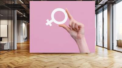 Woman's hand holding the female gender symbol of venus on pink background Wall mural