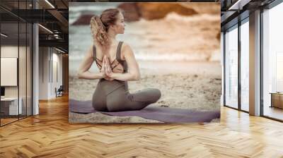 Woman doing yoga with namaste behind her back at beach, sitting in exercise, vajrasana pose Wall mural