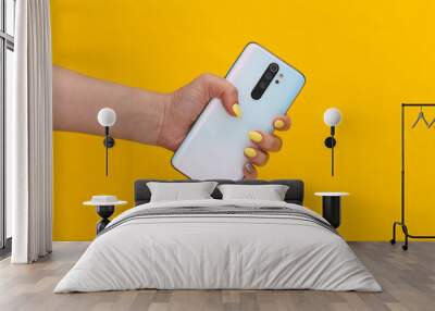 Woman hand holding modern smarphone on yellow background Wall mural