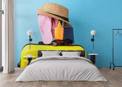 Yellow plastic travel suitcase with hat, passport and flip flops, sunblock on a yellow background. Tourism, summer vacation, beach resort, relocation concept Wall mural