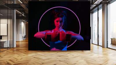 Young woman boxer with boxing gloves in a neon gradient red blue light on a dark background with glow circle. Wall mural