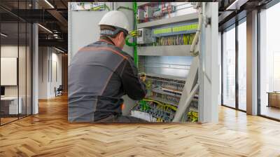 Electrician builder at work inspecting cabling connection of high voltage power electric line in industrial distribution fuseboard. Engineer works with electric cable wires of fuse switch box Wall mural